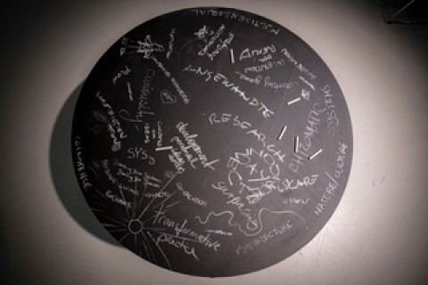 Eine dunkle runde Kreidetafel mit Wörtern und Zeichnungen
                           darauf