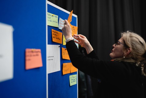 A woman is sticking a Post-it note on a bulletin board during a brainstorming session